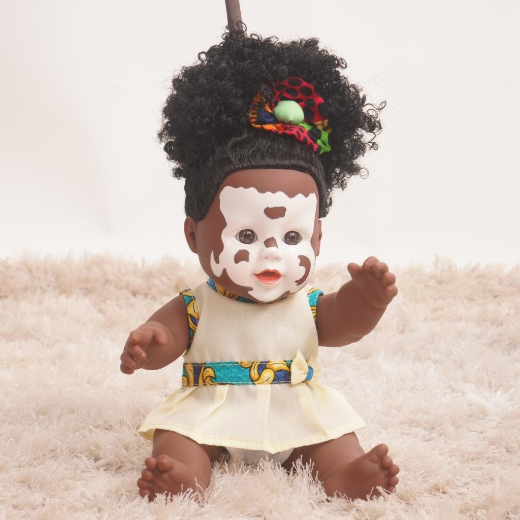 Baby doll with vitiligo skin and black hair sitting on carpet